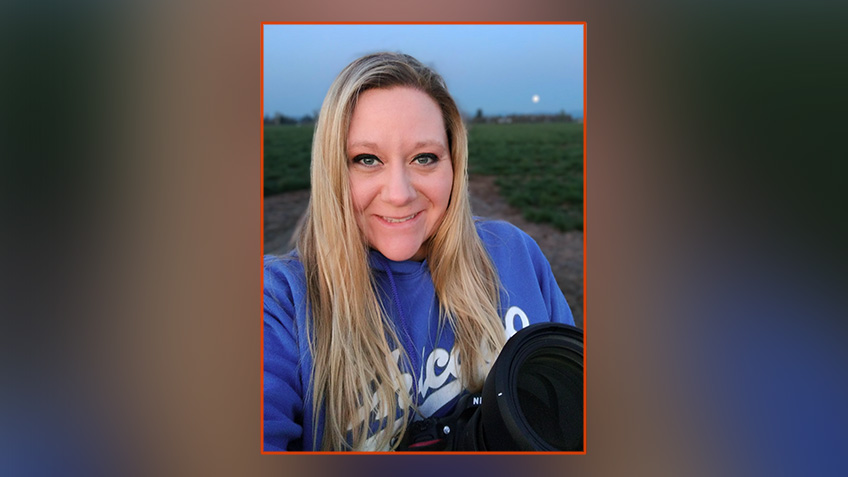 Melissa Whitney, an Oregon State University graduate and enrollment specialist, stands in a farm field at dusk holding a large lens camera.