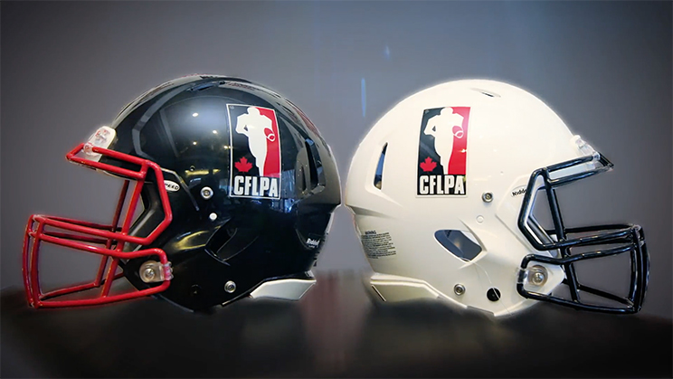 A black football helmet and a white football helmet, each bearing the logo for the Canadian Football League Players' Association, rest on a table. The CFLPA and Oregon State formed a collaboration to help professional football players earn their degrees online.